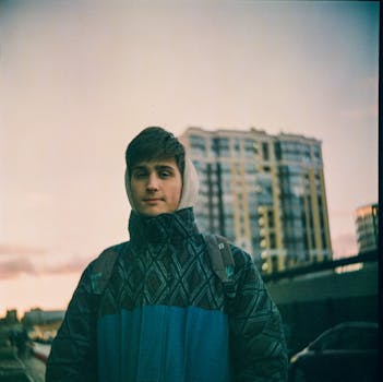Young man in hoodie and jacket standing outdoors during sunset in Saint Petersburg.