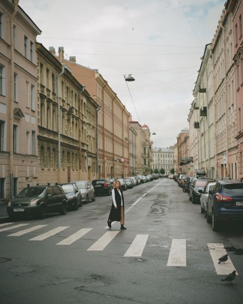 Free Woman crossing a street in Saint Petersburg lined with historical buildings and parked cars. Stock Photo
