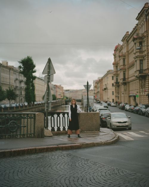 Free Woman stands on a St. Petersburg street by a canal, amidst historical buildings. Stock Photo