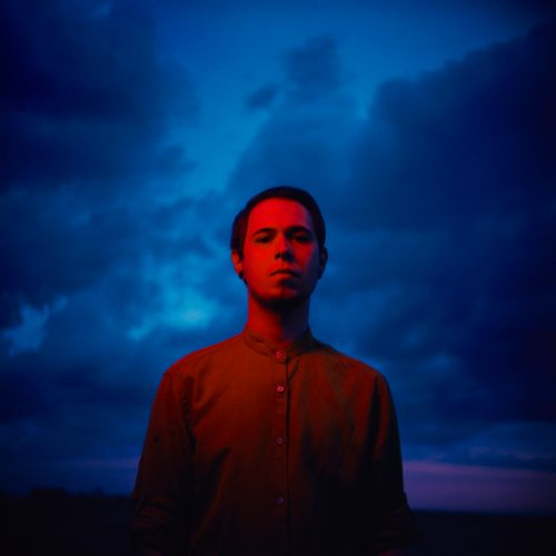 Free Portrait of a man illuminated by red light against a moody blue sky. Stock Photo