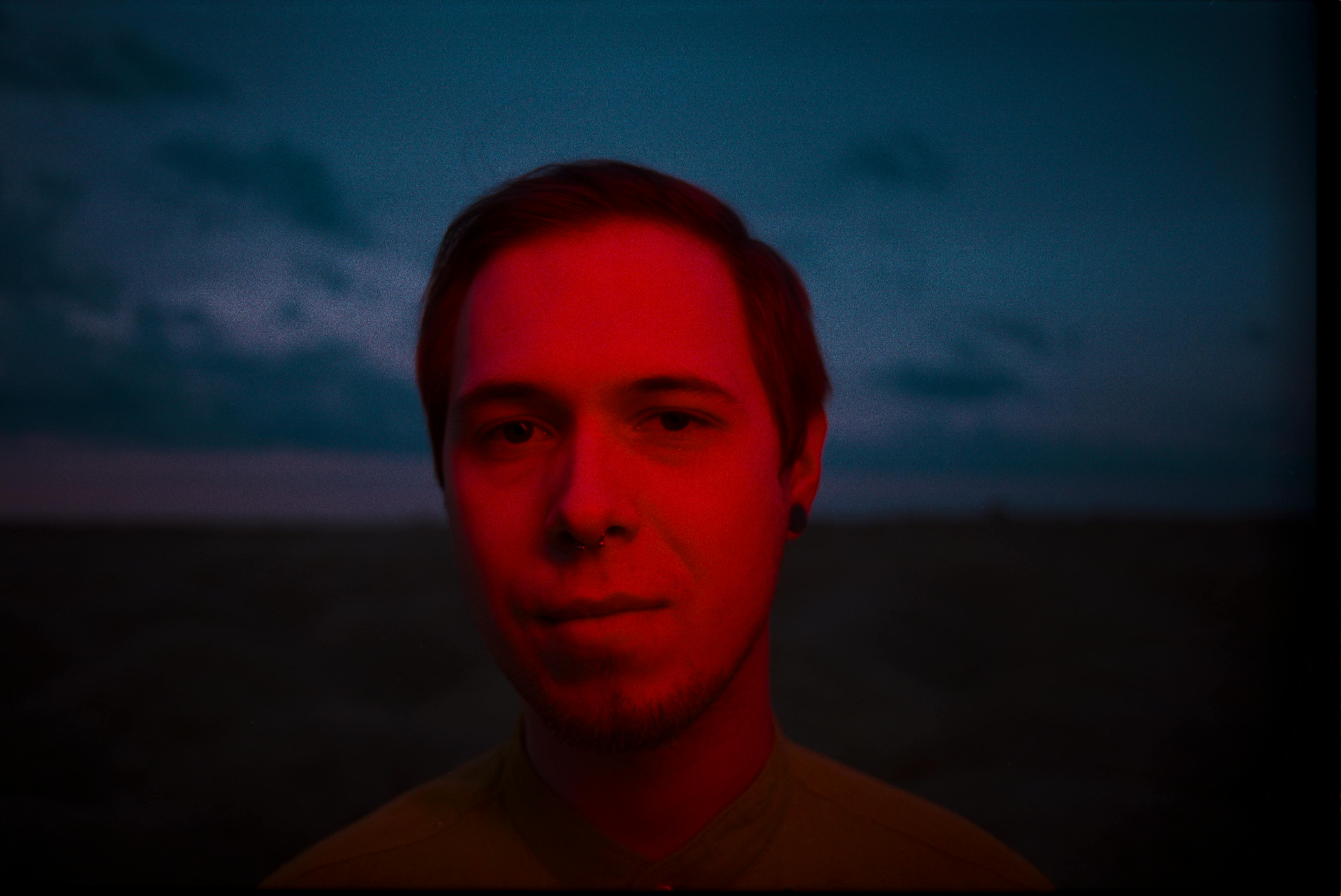 Atmospheric portrait of a young man illuminated by red light in a moody outdoor setting.