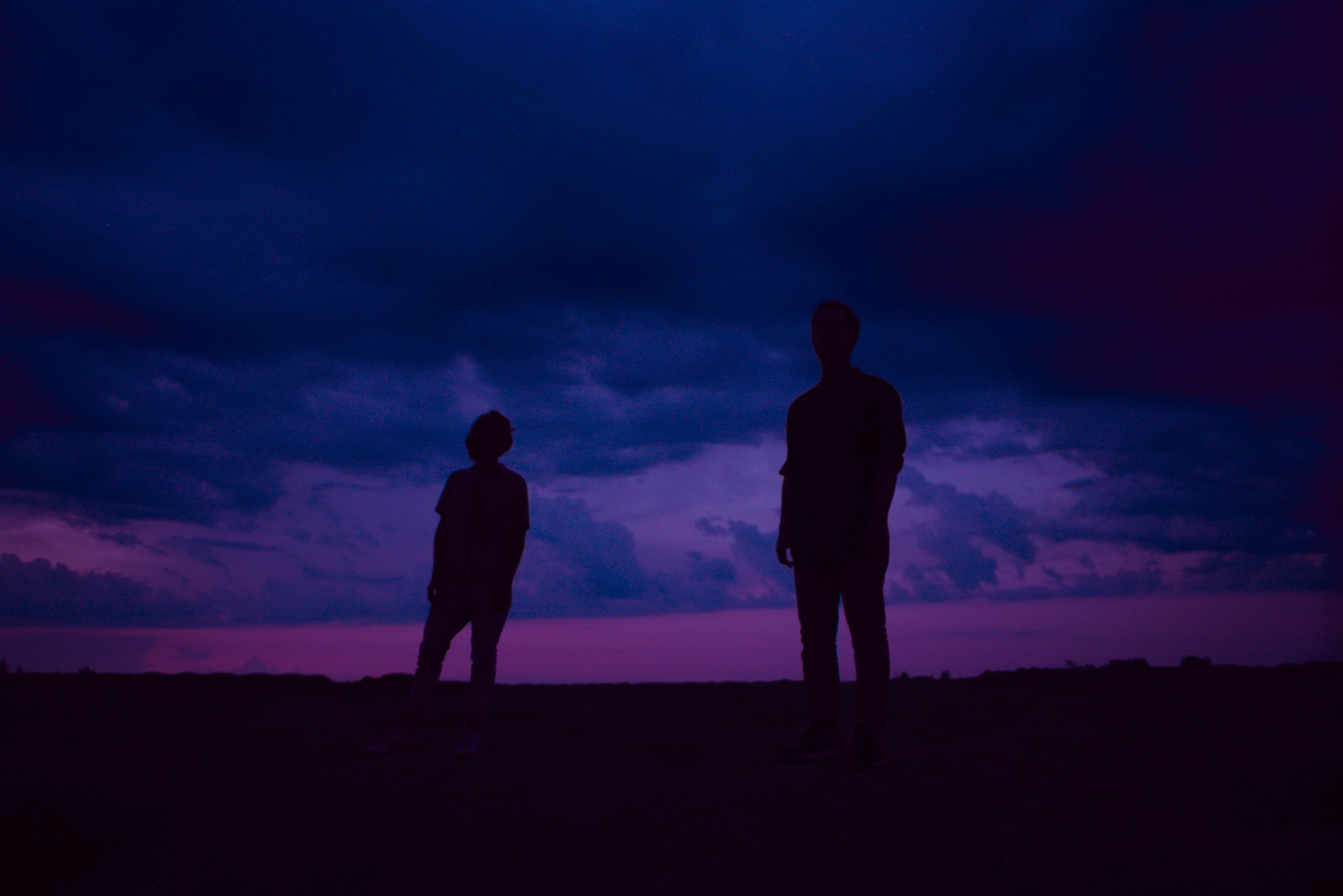 Two silhouettes stand beneath a dramatic twilight sky in a serene landscape.