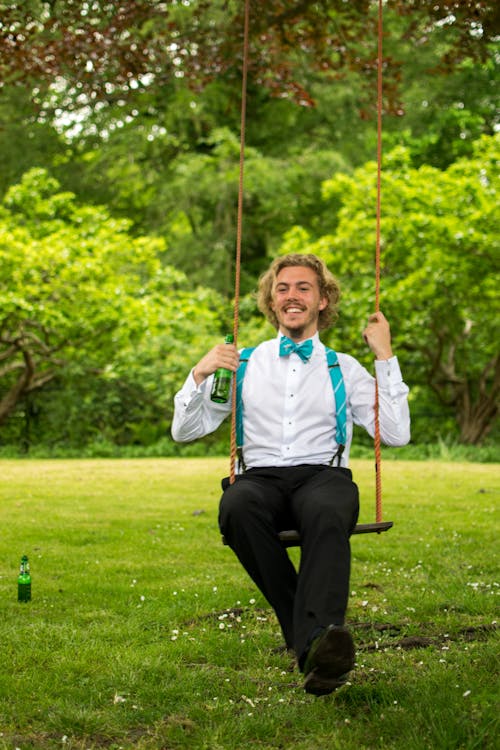 Man in White Dress Shirt and Black Pants Sitting on Swing