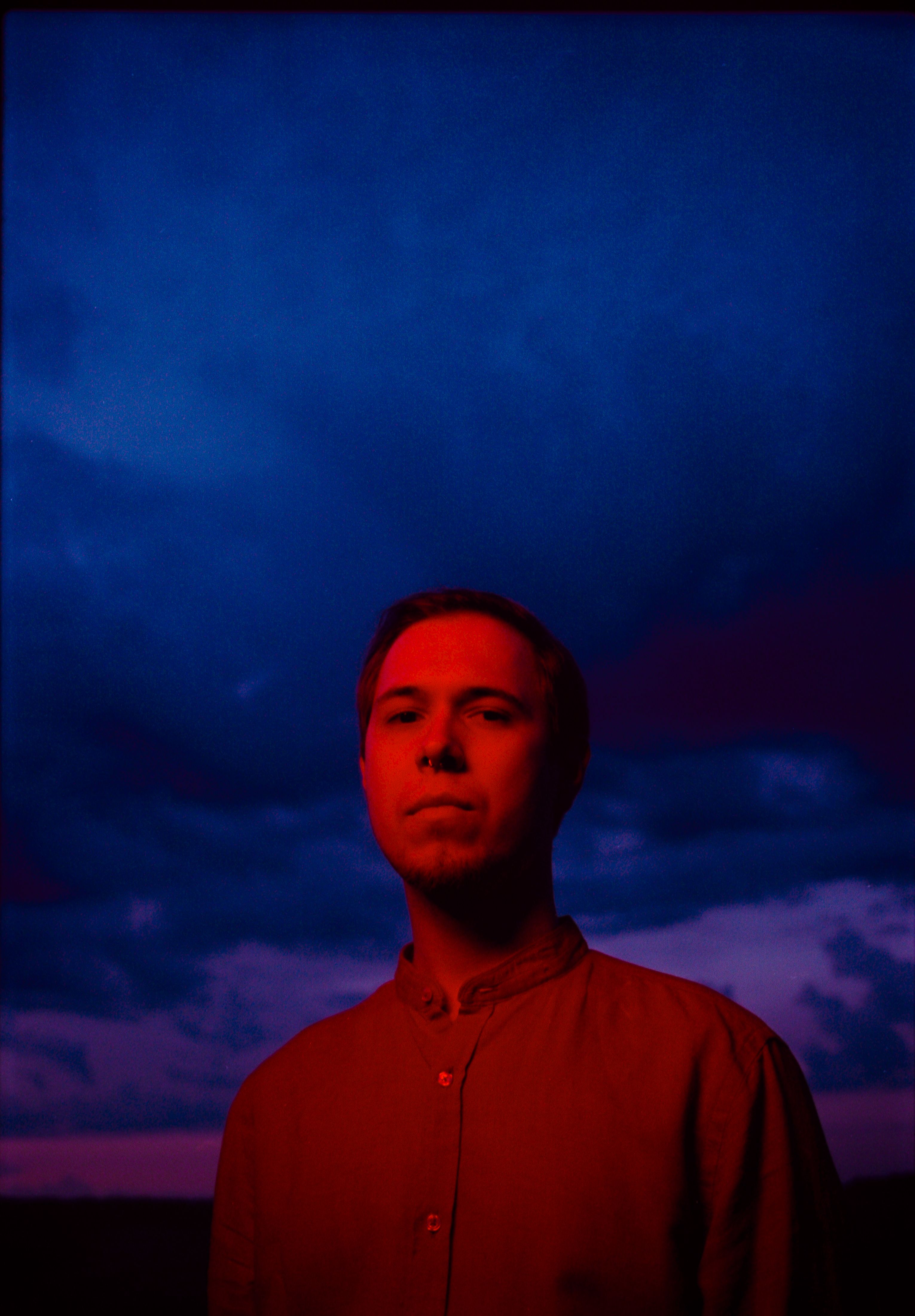 A moody portrait of a man under a striking blue and red evening sky in Saint Petersburg.