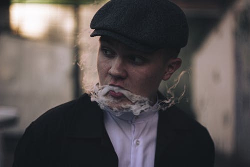 Photo of a Man with a Flat Cap Doing a Smoke Trick