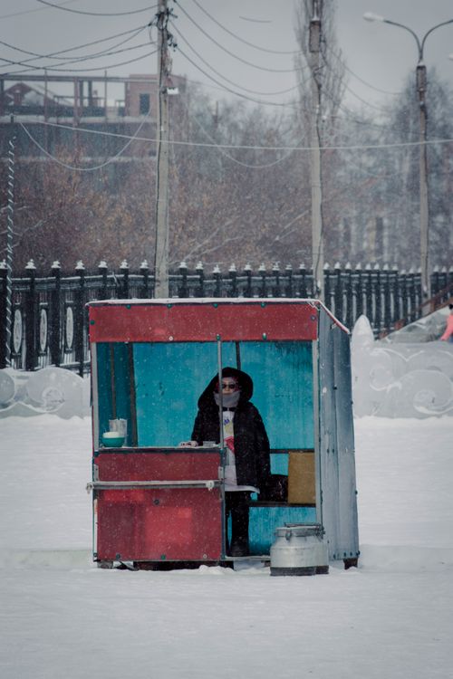 Free A street vendor stands in a snowy urban winter setting, selling goods. Stock Photo