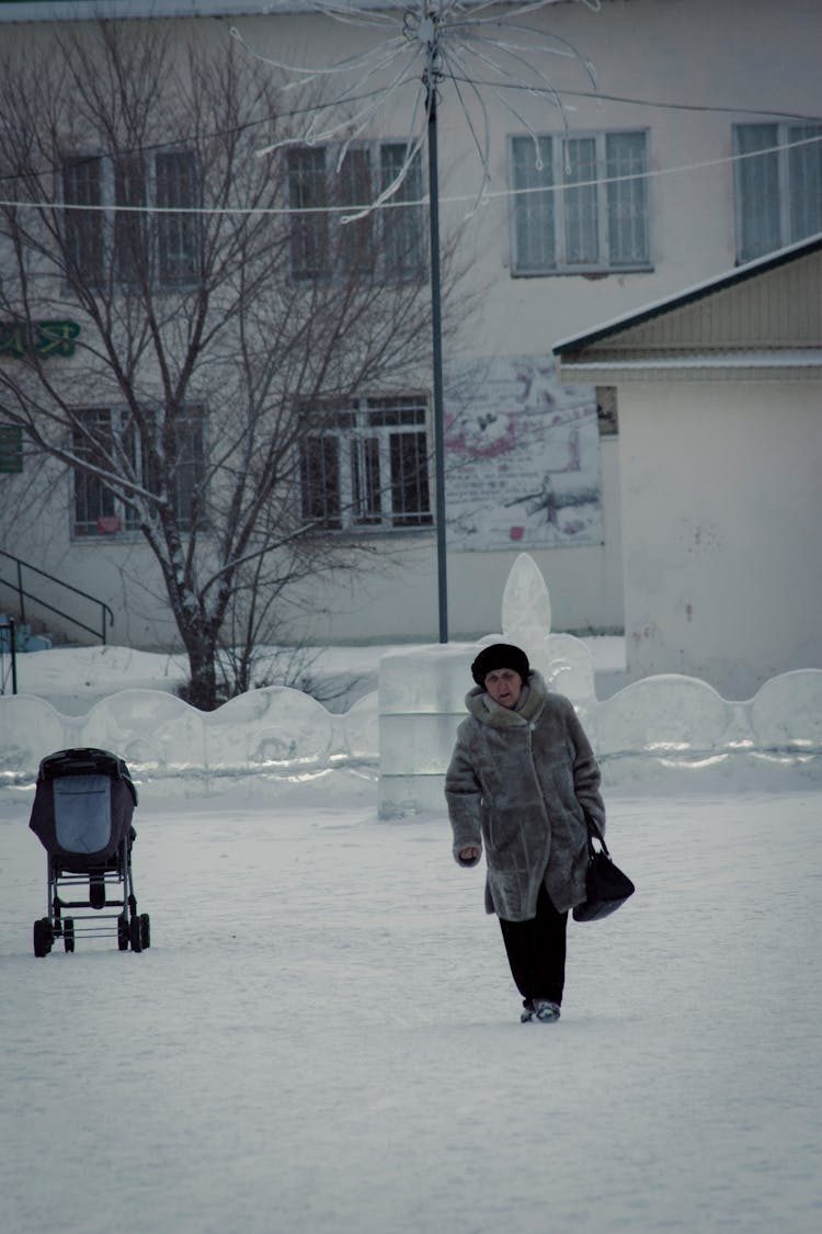 Photo Of An Elderly Woman In A Gray Jacket Walking On White Snow