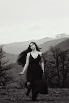 A blurred artistic shot of a woman in a black dress running in a mountainous landscape.