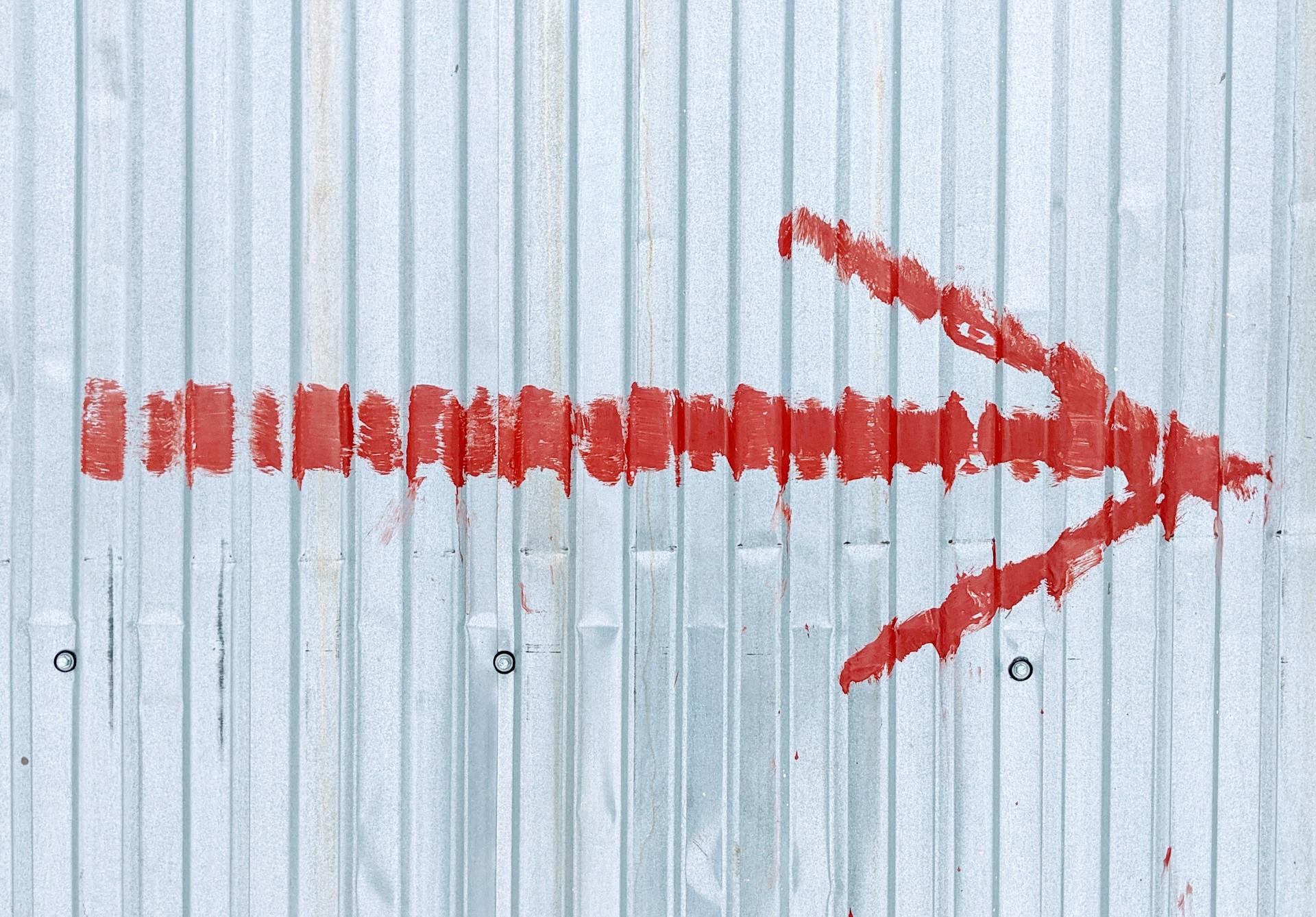 A vibrant red arrow painted on a corrugated metal wall directs attention to the right.