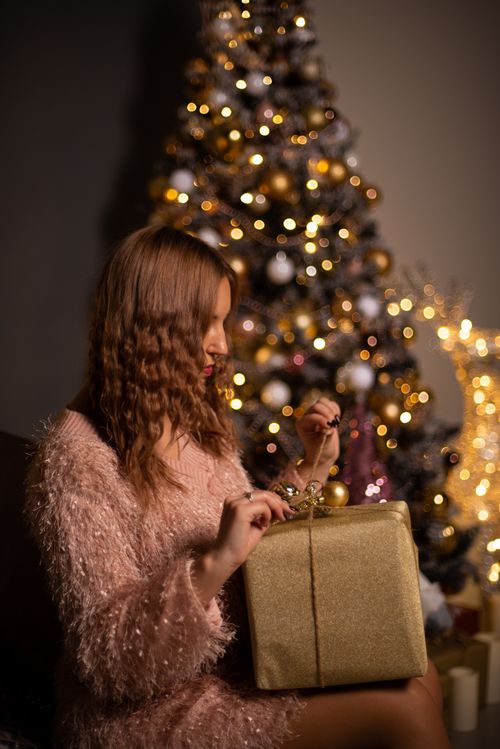 Free A woman unwraps a gift in front of a beautifully decorated Christmas tree, capturing the holiday spirit in Moscow. Stock Photo