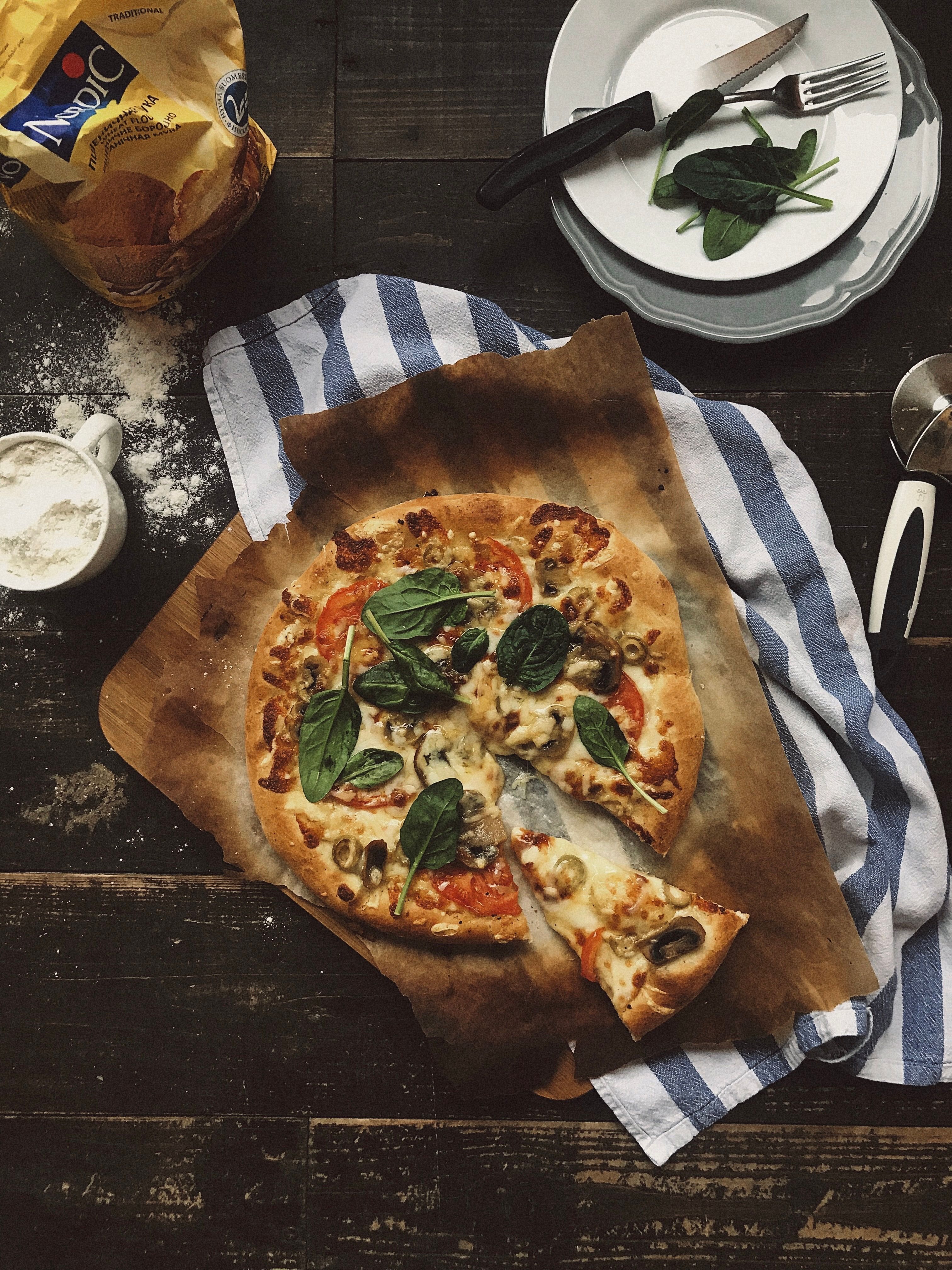 A delicious homemade pizza with fresh spinach and mushrooms on a rustic kitchen table.