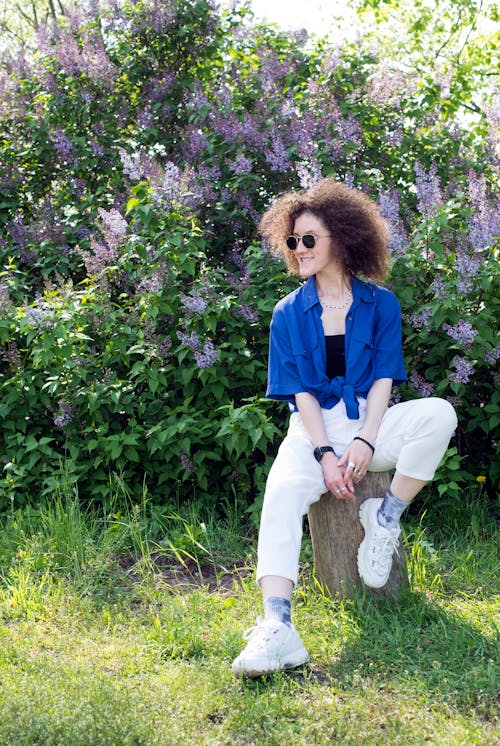 A Woman Wearing Sunglasses Sitting on a Log in a Garden