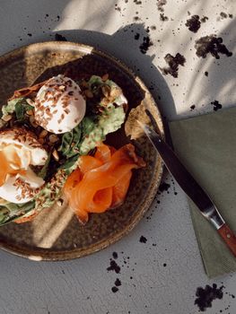 Delicious avocado toast with poached eggs and smoked salmon on a rustic plate.