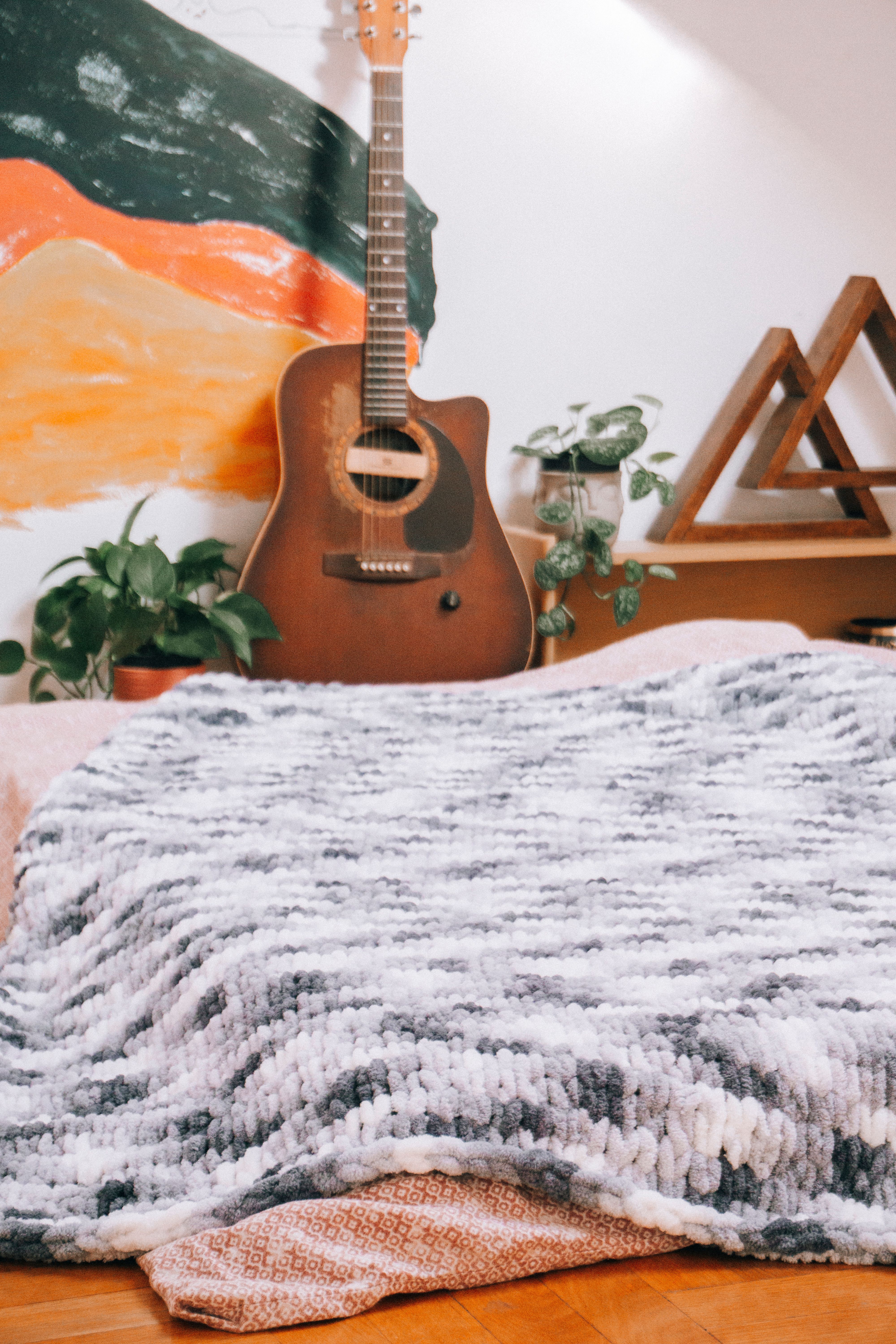 A cozy bedroom setup with a guitar, plants, and a textured blanket for relaxation.
