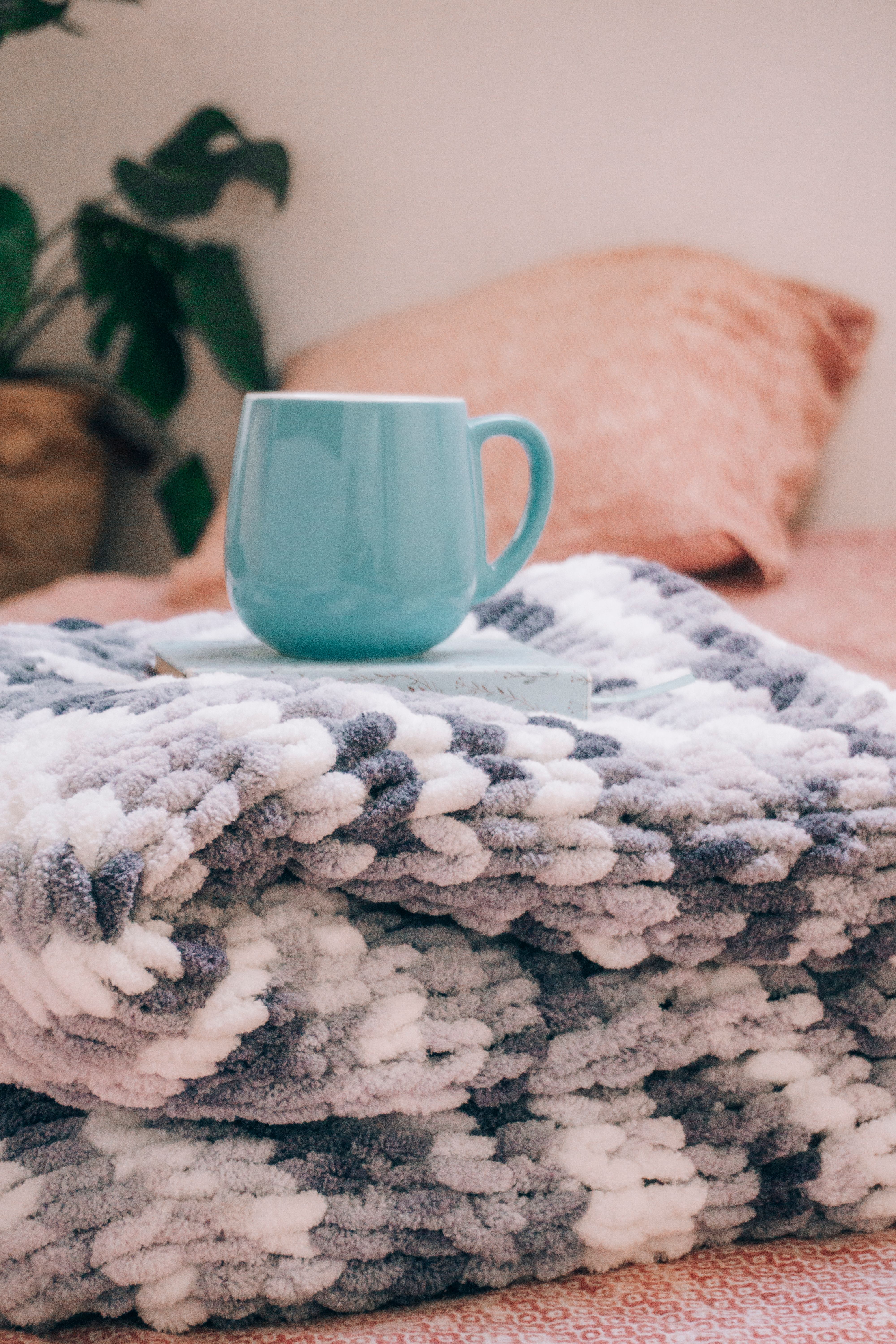 A cozy setup with a blue mug on a fluffy blanket indoors, evoking warmth and comfort.
