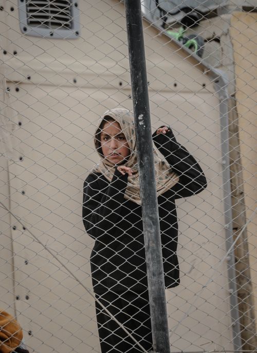 Free Middle Eastern woman stands behind a fence in Idlib, conveying resilience and struggle. Stock Photo