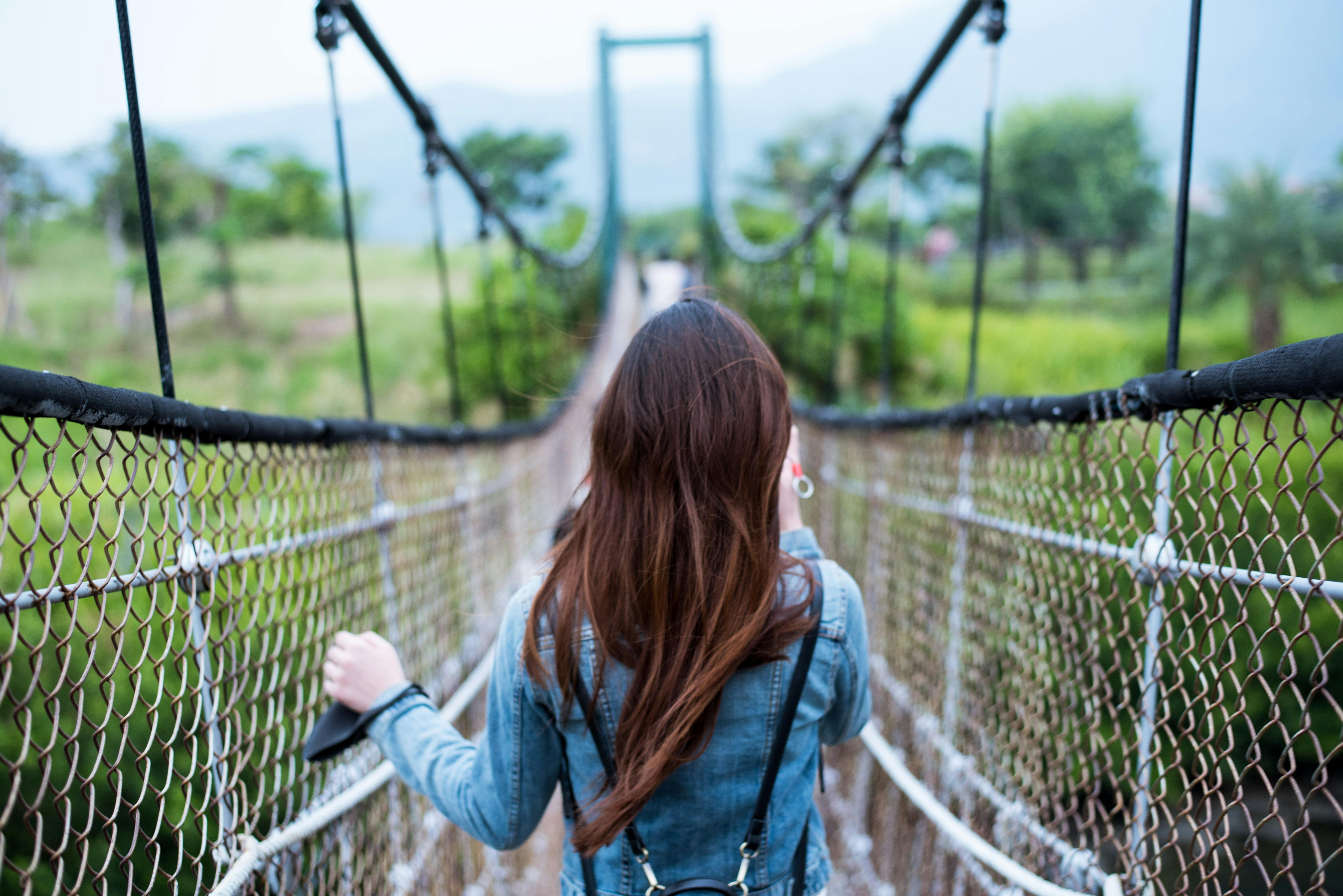 woman in blue long sleeved dress on rope bridge