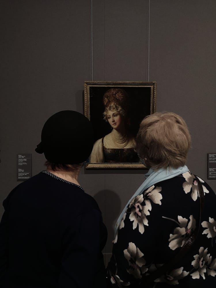 Women Looking At A Portrait Hanging On A Wall