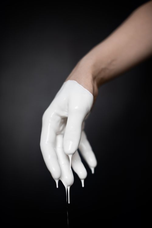 Free A close-up image of a human hand coated and dripping with white paint against a dark background. Stock Photo