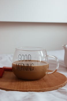 Glass mug of coffee labeled 'Good Morning' on a tray in a cozy setting.