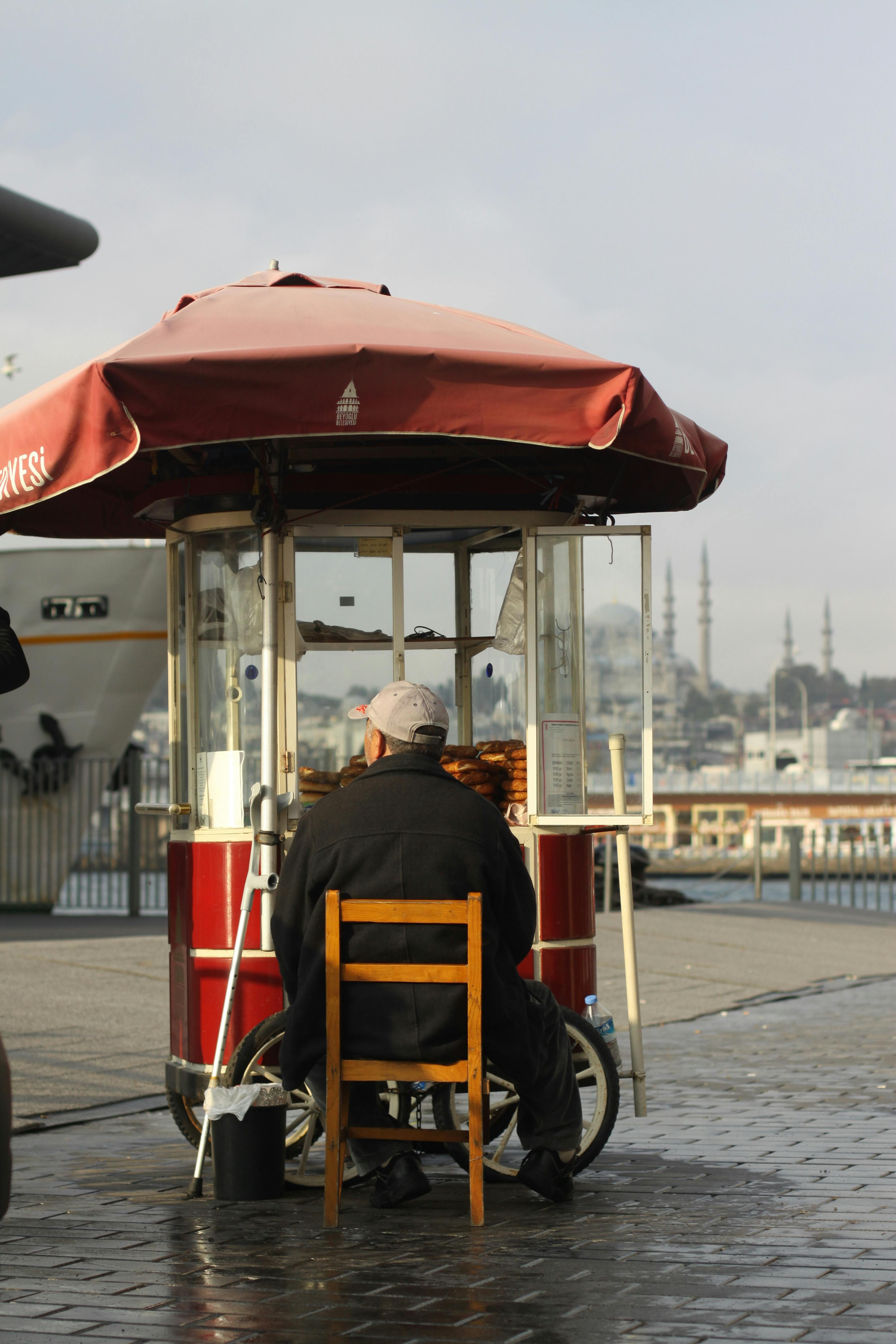A street vendor selling goods from a red cart near a historic mosque on a sunny day.