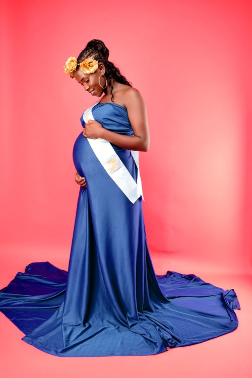 Free Pregnant woman in a flowing blue gown with floral accents on a pink backdrop. Stock Photo