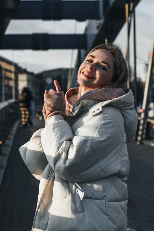 Free A cheerful woman in a winter coat smiles on a city bridge during daytime. Stock Photo