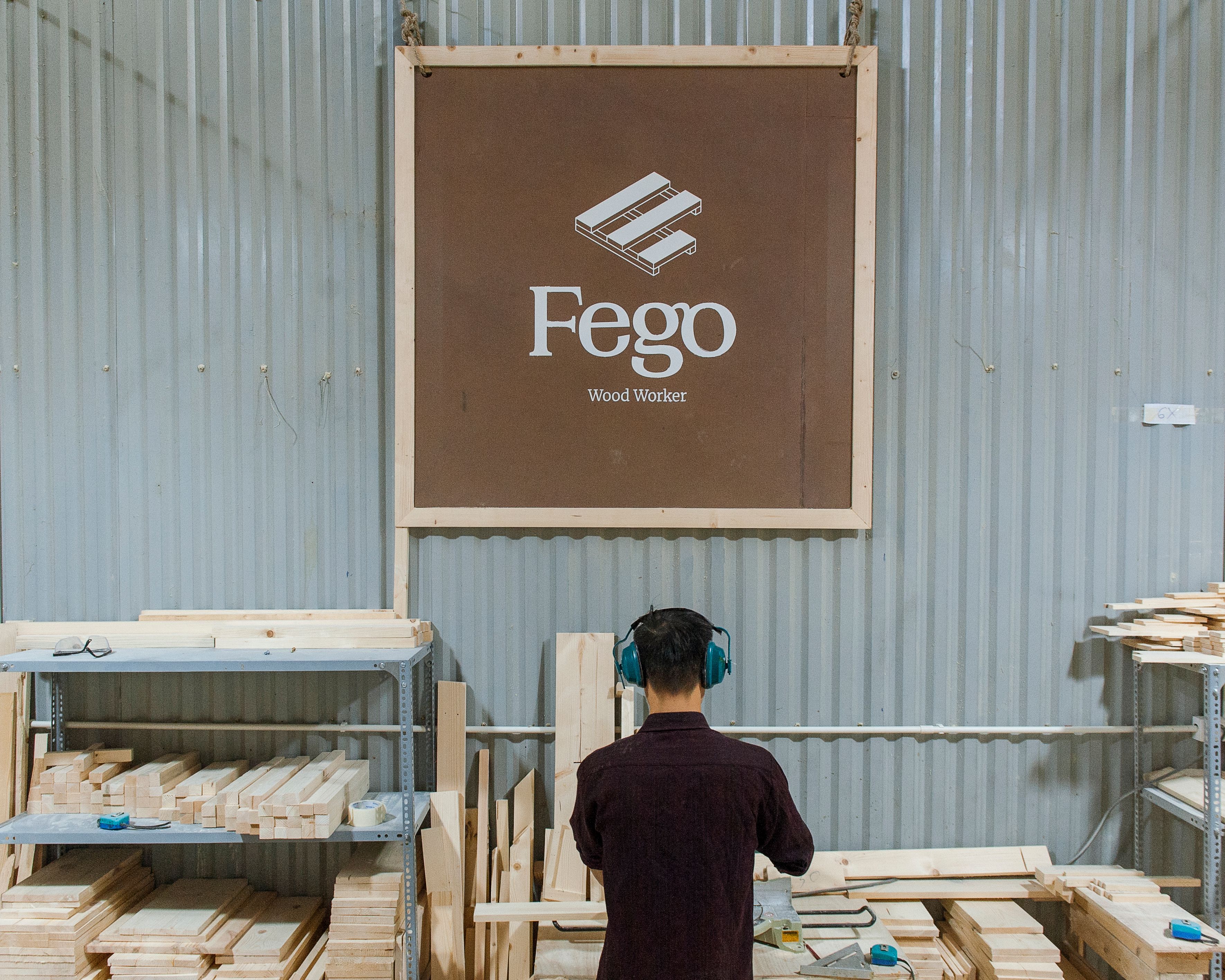 Man working in a wood workshop with safety headphones. Fego Wood Worker sign in background.