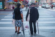 Two senior adults crossing a busy street in downtown Los Angeles, showcasing urban life.