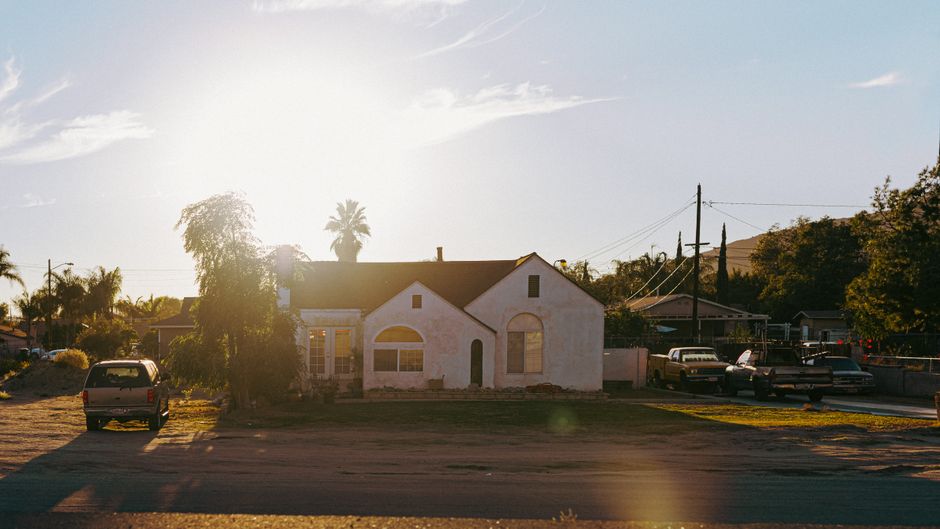A picturesque suburban house with a sunlit facade and vintage cars in the foreground.