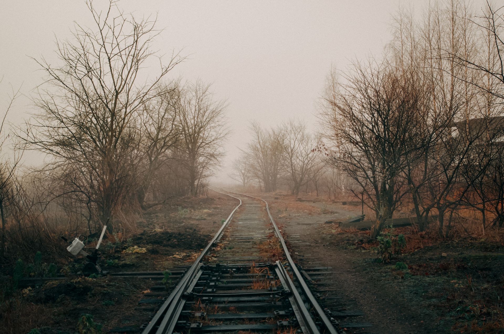 Railroad tracks leading through a misty and foggy countryside landscape, flanked by bare winter trees.