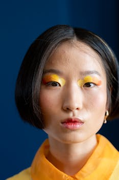 Close-up portrait of woman with bold yellow and orange makeup against a blue background.