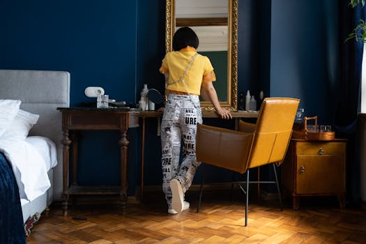 A stylish woman in a yellow top intently looks into a large mirror in a chic, blue-themed room.