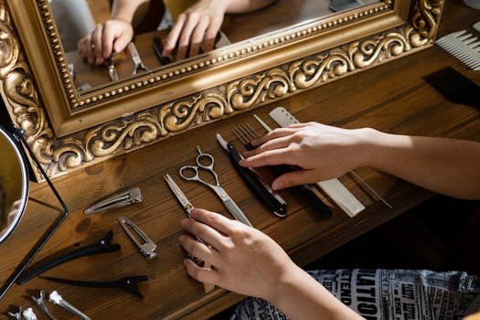 Hands arranging hair styling tools on a wooden table near a decorative mirror.