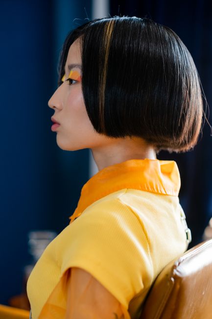 Profile of a woman with creative makeup and modern haircut in vibrant attire.