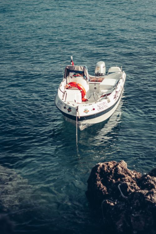 Free White boat tied to the rocky shore in Antalya's serene blue sea, capturing tranquility. Stock Photo