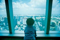 一个年幼的孩子透过一扇大窗户，俯瞰着曼谷的天际线，将城市全景尽收眼底