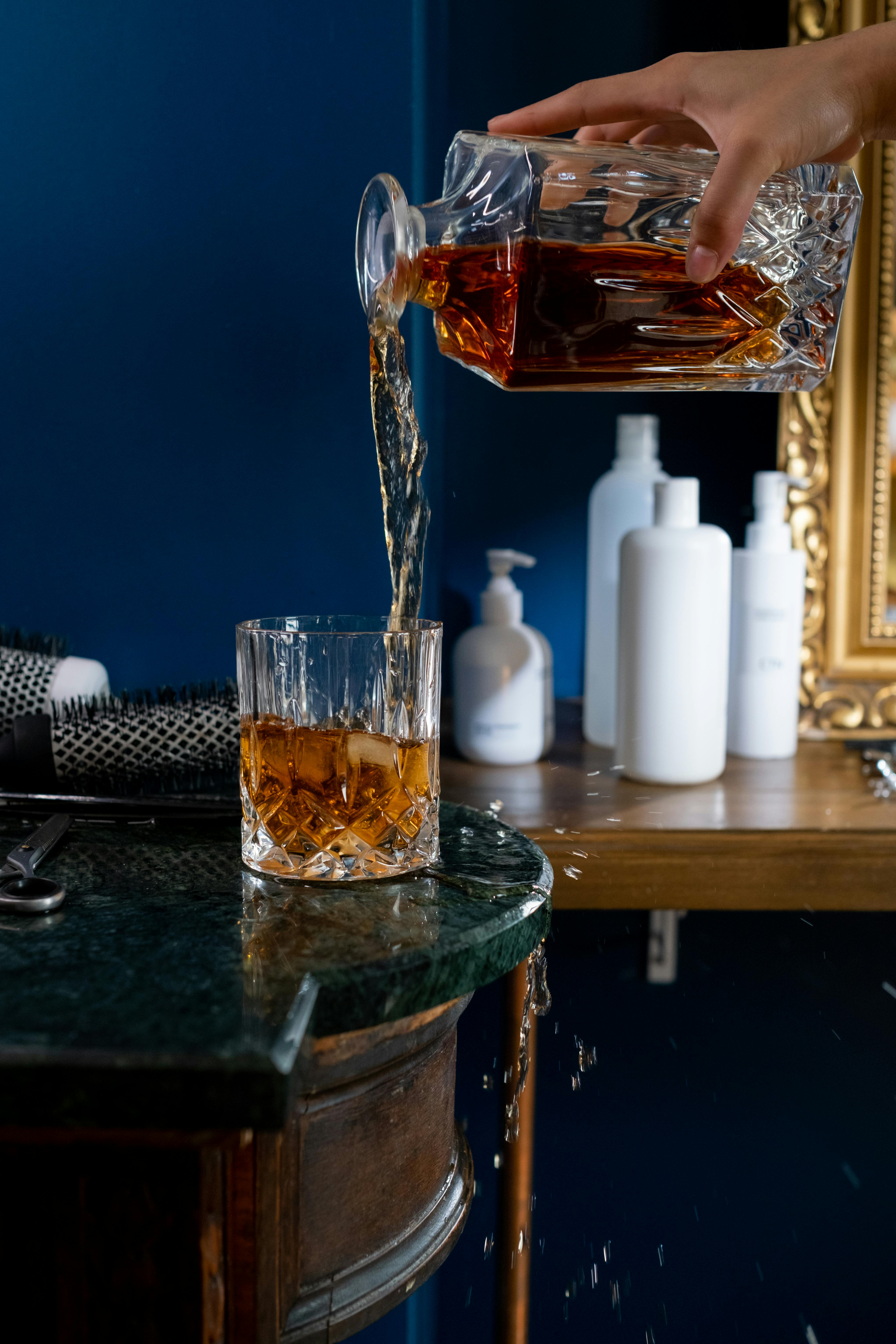 A hand pouring whiskey from a decanter into a glass on a stylish table, showcasing elegance.