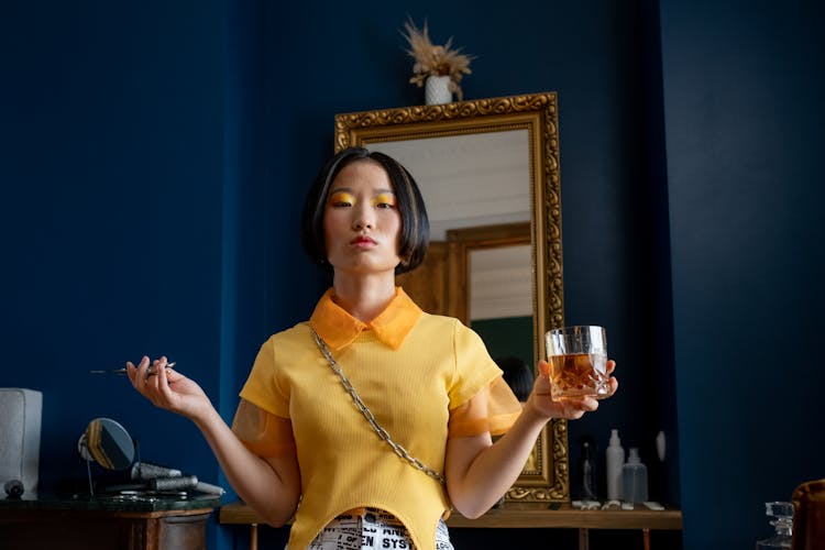 Woman Holding Whiskey Glass And Scissors Standing In Front Of Mirror