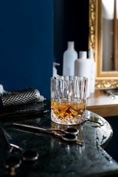 Crystal glass of whiskey on a salon table with scissors and brushes, exuding elegance and sophistication.