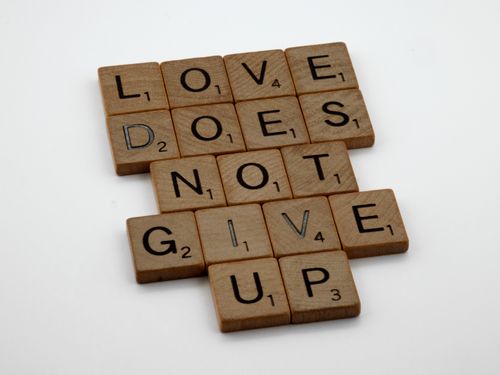 Free Wooden tiles on a white surface spell 'Love does not give up' in a motivational layout. Stock Photo