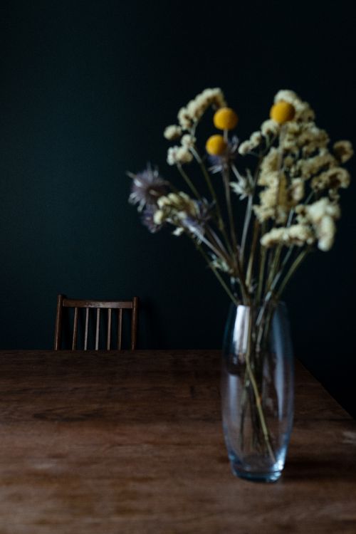 Free A beautiful floral arrangement in a glass vase with a rustic chair and table set against a dark backdrop. Stock Photo