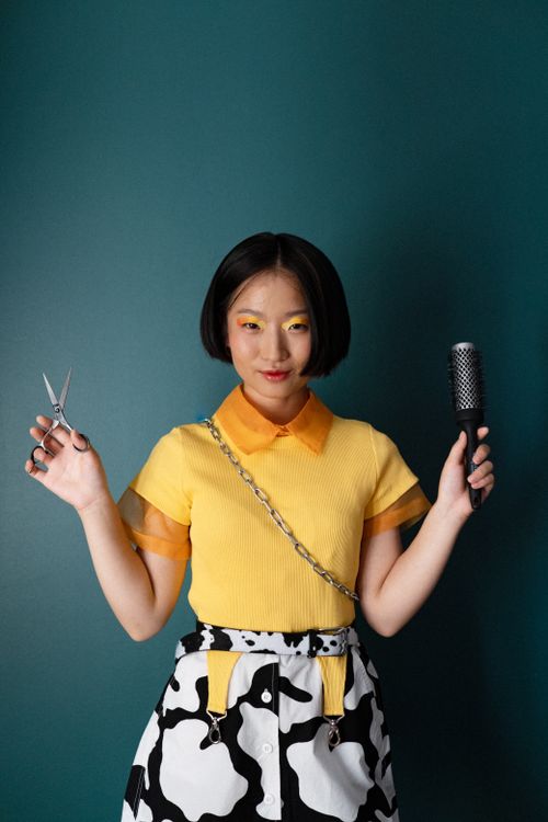 Free Young woman with scissors and hairbrush against green background, fashion concept. Stock Photo
