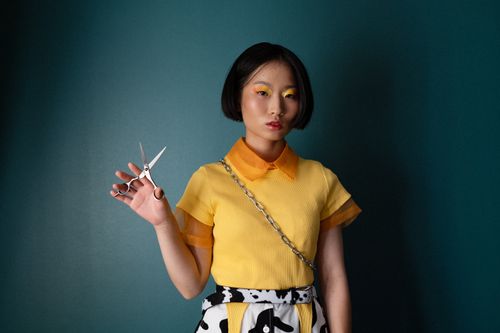 Free Chic woman in colorful outfit holding scissors against a dark backdrop, exuding modern fashion. Stock Photo