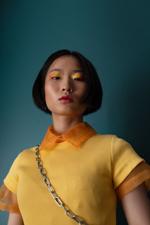 Free Portrait of a woman in a yellow blouse against a teal backdrop with vibrant makeup. Stock Photo