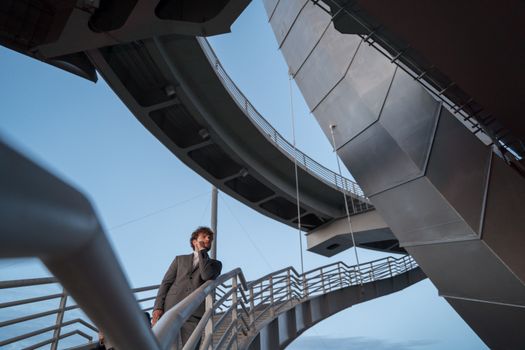 Caucasian man in suit with hand on chin, standing on modern architectural bridge at dusk.