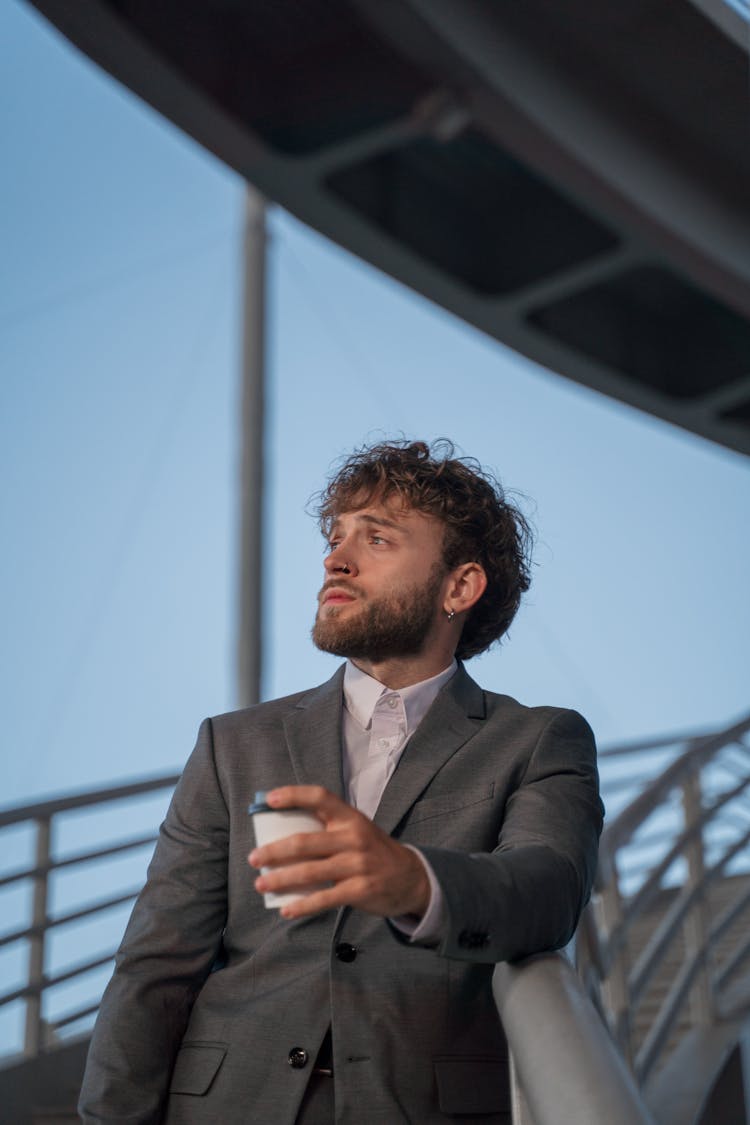 Man In A Gray Suit Looking Away While Holding A Cup Of Coffee