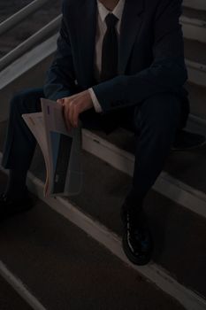 Adult male holding newspaper while seated on outdoor stairs at night.