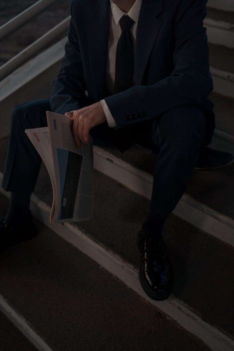 Man In A Suit Sitting Holding Newspaper