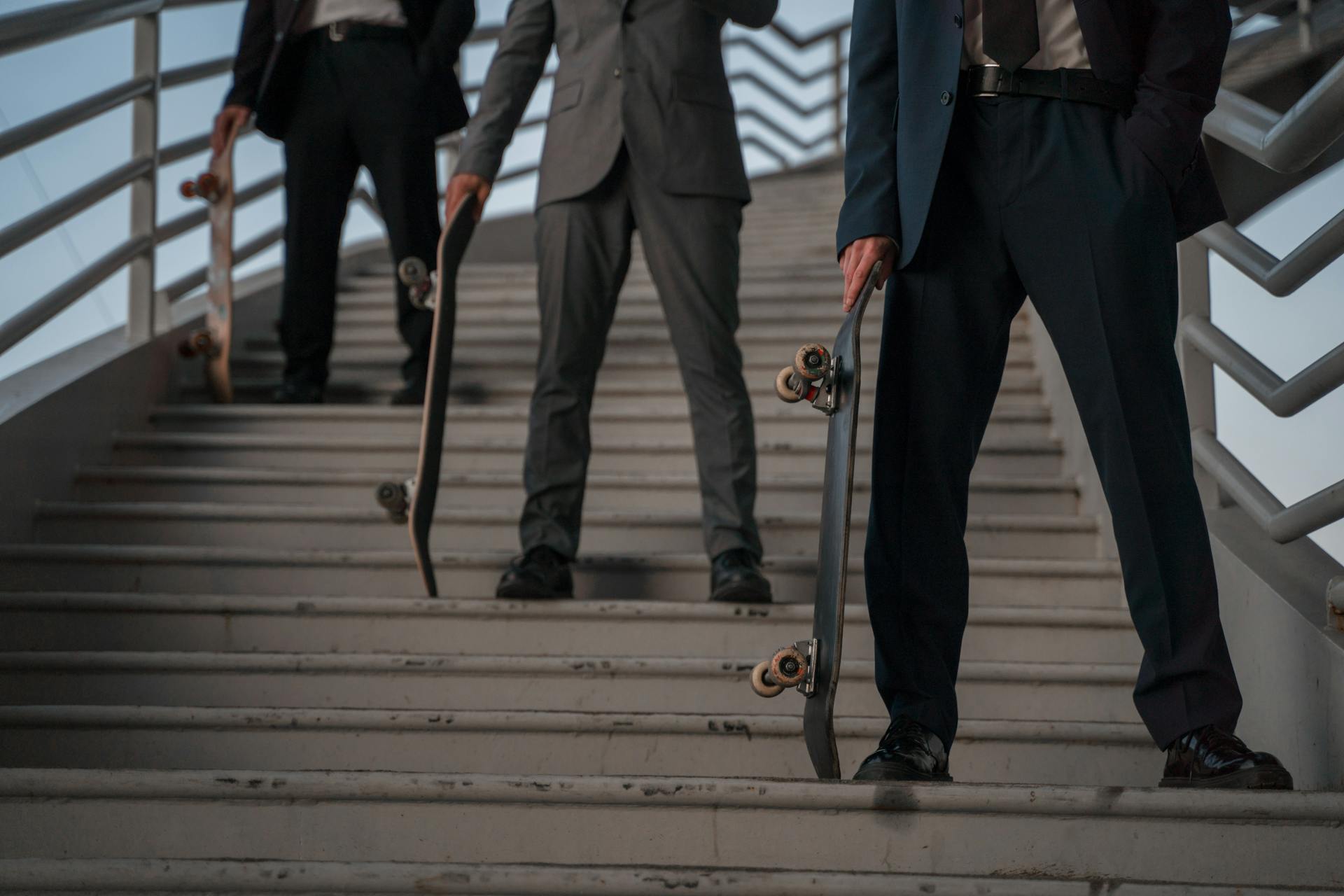 Men in suits holding skateboards on stairs, blending business and skateboard culture.